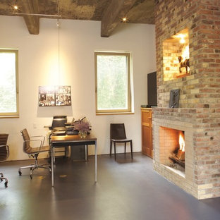 Large modern study in New York with white walls, concrete flooring, a standard fireplace, a brick fireplace surround, a freestanding desk and grey floors.
