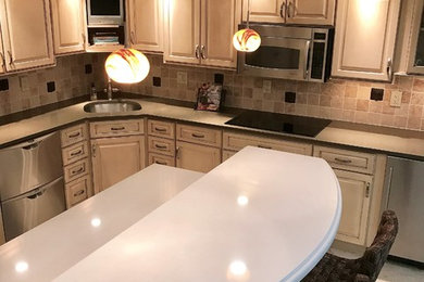 Example of a mid-sized transitional l-shaped travertine floor and beige floor eat-in kitchen design in Other with an undermount sink, raised-panel cabinets, beige cabinets, quartz countertops, beige backsplash, travertine backsplash, stainless steel appliances and an island