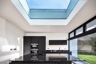Inspiration for a medium sized contemporary single-wall kitchen/diner in Cork with a submerged sink, flat-panel cabinets, black cabinets, engineered stone countertops, black splashback, engineered quartz splashback, black appliances, medium hardwood flooring, an island, brown floors and black worktops.