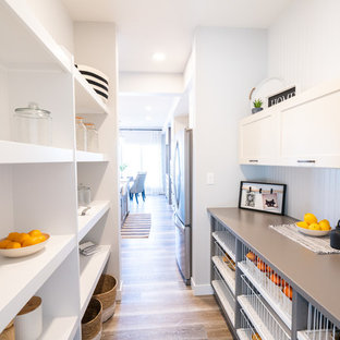 Cette photo montre une arrière-cuisine parallèle chic de taille moyenne avec un placard à porte shaker, des portes de placard blanches, un plan de travail en quartz modifié, une crédence blanche, une crédence en bois, un sol en bois brun, aucun îlot, un sol marron et un plan de travail gris.