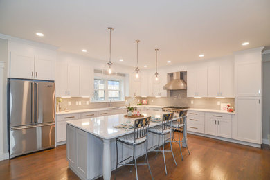 Inspiration for a large transitional l-shaped medium tone wood floor and brown floor eat-in kitchen remodel in Boston with a drop-in sink, shaker cabinets, white cabinets, quartz countertops, gray backsplash, ceramic backsplash, stainless steel appliances, an island and white countertops
