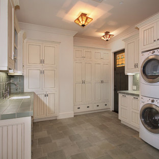 Photo of an expansive traditional u-shaped separated utility room in San Diego with recessed-panel cabinets, white walls, a stacked washer and dryer, grey floors, a submerged sink, tile countertops, slate flooring, green worktops and beige cabinets.