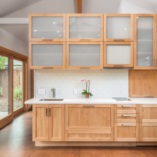 Новый формат декора квартиры: маленькая линейная кухня-гостиная в современном стиле с пробковым полом, одинарной раковиной, стеклянными фасадами, светлыми деревянными фасадами, столешницей из гранита, белым фартуком, техникой из нержавеющей стали, фартуком из плитки кабанчик и коричневым полом без острова