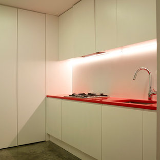 Design ideas for a medium sized contemporary l-shaped laundry cupboard in London with a built-in sink, flat-panel cabinets, white cabinets, composite countertops, white walls, concrete flooring, a stacked washer and dryer, grey floors and red worktops.