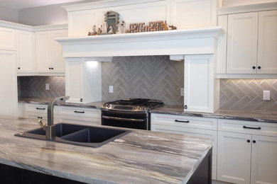Example of a large transitional l-shaped medium tone wood floor and brown floor kitchen design in Other with no island, a drop-in sink, recessed-panel cabinets, white cabinets, gray backsplash, porcelain backsplash and stainless steel appliances