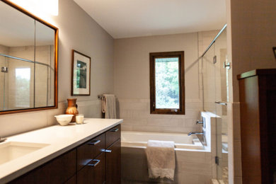 This is an example of a small contemporary master bathroom in Minneapolis with flat-panel cabinets, dark wood cabinets, engineered quartz benchtops, white benchtops, a drop-in tub, a corner shower, gray tile, grey walls, an undermount sink, grey floor and a hinged shower door.