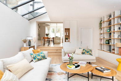 This is an example of a large contemporary formal open plan living room feature wall in London with blue walls, light hardwood flooring, a wall mounted tv and beige floors.