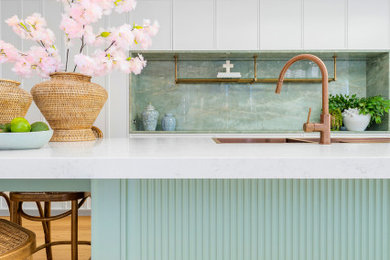 Photo of a large transitional galley open plan kitchen in Sydney with a double-bowl sink, recessed-panel cabinets, green cabinets, quartz benchtops, green splashback, stone slab splashback, light hardwood floors, with island and white benchtop.