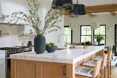 Example of a beach style galley light wood floor, beige floor and exposed beam kitchen design in Boston with shaker cabinets, white cabinets, white backsplash, stainless steel appliances, an island and white countertops