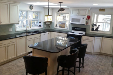 Example of a large transitional l-shaped vinyl floor, gray floor and tray ceiling kitchen pantry design in Manchester with a double-bowl sink, shaker cabinets, white cabinets, granite countertops, green backsplash, porcelain backsplash, stainless steel appliances, an island and black countertops
