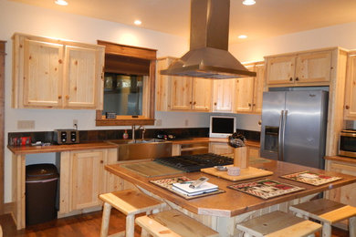 Kitchen - large rustic l-shaped medium tone wood floor kitchen idea in Boise with a farmhouse sink, recessed-panel cabinets, light wood cabinets, laminate countertops, brown backsplash, ceramic backsplash, stainless steel appliances and an island