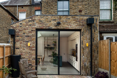 This is an example of a medium sized contemporary brick and rear house exterior in London with three floors and a flat roof.