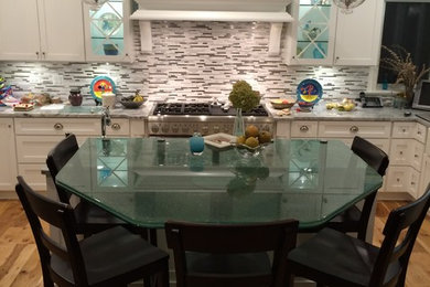 Example of a mid-sized classic u-shaped light wood floor eat-in kitchen design in Chicago with a farmhouse sink, flat-panel cabinets, white cabinets, glass countertops, gray backsplash, glass tile backsplash, stainless steel appliances and an island