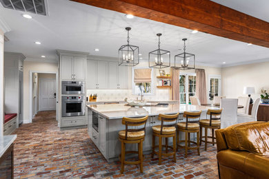 Example of a mid-sized classic l-shaped brick floor and brown floor open concept kitchen design in New Orleans with an undermount sink, recessed-panel cabinets, beige cabinets, quartzite countertops, white backsplash, ceramic backsplash, stainless steel appliances, an island and white countertops