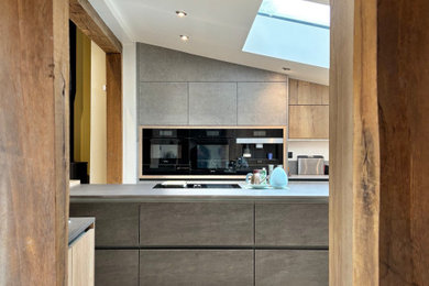 Example of a large urban u-shaped limestone floor, beige floor and vaulted ceiling eat-in kitchen design in Other with an integrated sink, flat-panel cabinets, gray cabinets, black appliances, an island and gray countertops