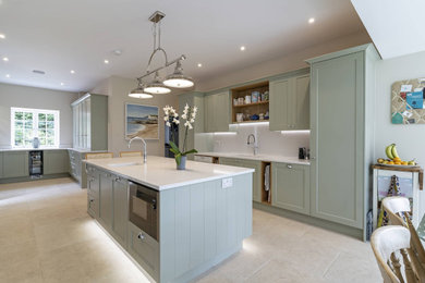 Small contemporary u-shaped kitchen/diner in Oxfordshire with a built-in sink, shaker cabinets, green cabinets, quartz worktops, white splashback, black appliances, ceramic flooring, an island, brown floors, white worktops and feature lighting.