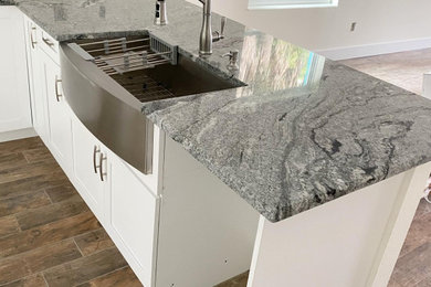 Example of a mid-sized minimalist l-shaped eat-in kitchen design in Tampa with a farmhouse sink, shaker cabinets, white cabinets, granite countertops, stainless steel appliances and gray countertops