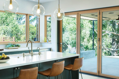 Large modern open plan kitchen in San Francisco with a farmhouse sink, shaker cabinets, blue cabinets, quartz benchtops, white splashback, ceramic splashback, stainless steel appliances, light hardwood floors, with island and white benchtop.