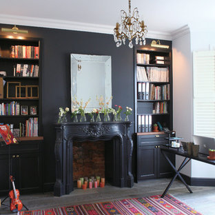 This is an example of a traditional home office in London with black walls, dark hardwood floors, a standard fireplace, a plaster fireplace surround, a freestanding desk and black floor.
