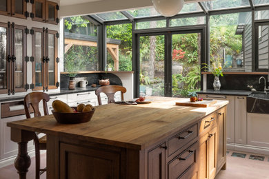 Example of a large eclectic medium tone wood floor enclosed kitchen design in Seattle with a farmhouse sink, glass-front cabinets, white cabinets, soapstone countertops, black backsplash, stone slab backsplash and black countertops