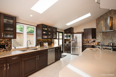 This is an example of a large transitional u-shaped eat-in kitchen in Dallas with a double-bowl sink, glass-front cabinets, dark wood cabinets, brown splashback, stainless steel appliances, porcelain floors, with island, quartz benchtops and glass tile splashback.