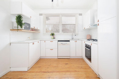 Photo of a mid-sized scandinavian u-shaped separate kitchen in Newcastle - Maitland with a single-bowl sink, laminate benchtops, white splashback, subway tile splashback, stainless steel appliances, light hardwood floors, no island, brown floor and white benchtop.