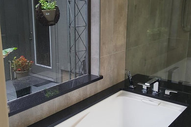 Tub/shower combo - large modern master beige tile and ceramic tile ceramic tile and gray floor tub/shower combo idea in Houston with flat-panel cabinets, gray cabinets, an undermount tub, a two-piece toilet, beige walls, an undermount sink, granite countertops, a hinged shower door and black countertops