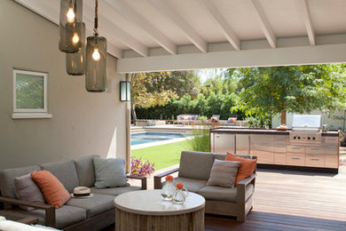This is an example of an expansive midcentury backyard patio in Los Angeles with an outdoor kitchen, decking and a roof extension.