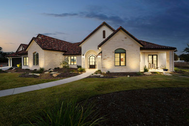 Large elegant white one-story stone house exterior photo in Austin with a tile roof and a brown roof