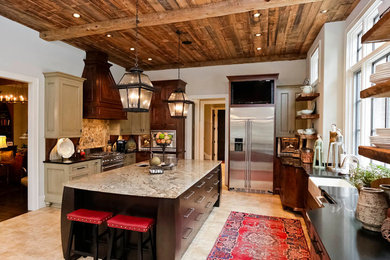 Inspiration for a large rustic l-shaped travertine floor enclosed kitchen remodel in Other with recessed-panel cabinets, stainless steel appliances, an island, a farmhouse sink, beige cabinets, granite countertops, beige backsplash and stone tile backsplash