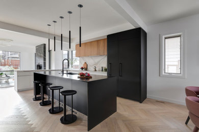 Inspiration for a mid-sized contemporary galley light wood floor eat-in kitchen remodel in Calgary with an undermount sink, flat-panel cabinets, black cabinets, quartz countertops, white backsplash, quartz backsplash, paneled appliances, an island and white countertops