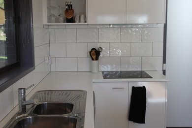 Photo of a small modern u-shaped open plan kitchen in Melbourne with a double-bowl sink, flat-panel cabinets, white cabinets, laminate benchtops, white splashback, ceramic splashback, stainless steel appliances, ceramic floors, a peninsula, grey floor and white benchtop.
