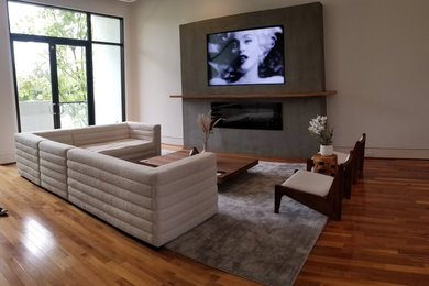 Example of a mid-sized trendy enclosed medium tone wood floor and multicolored floor living room design in Houston with a bar, gray walls, a concrete fireplace and a media wall