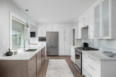 This is an example of a mid-sized transitional galley eat-in kitchen in Vancouver with flat-panel cabinets, white cabinets, quartz benchtops, grey splashback, glass sheet splashback, stainless steel appliances, white benchtop, an undermount sink, medium hardwood floors and brown floor.
