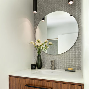 Photo of a mid-sized contemporary bathroom in New York with furniture-like cabinets, brown cabinets, a one-piece toilet, metal tile, white walls, porcelain floors, an undermount sink, grey floor, white benchtops, a single vanity and a floating vanity.