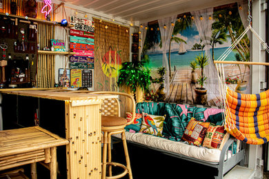 Imagen de bar en casa con barra de bar en L tropical pequeño con armarios abiertos, puertas de armario de madera clara, encimera de madera, suelo de madera pintada y suelo negro