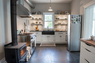 This is an example of a small transitional u-shaped separate kitchen in Toronto with a farmhouse sink, beaded inset cabinets, white cabinets, soapstone benchtops, white splashback, subway tile splashback, stainless steel appliances and slate floors.