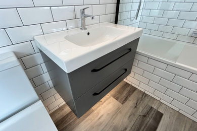 Photo of a small modern grey and white family bathroom in Hampshire with flat-panel cabinets, grey cabinets, a built-in bath, a shower/bath combination, a two-piece toilet, black and white tiles, porcelain tiles, white walls, vinyl flooring, an integrated sink, grey floors, a hinged door, a laundry area, a single sink and a floating vanity unit.