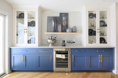 Mid-sized transitional single-wall brown floor and medium tone wood floor home bar photo in New York with shaker cabinets, quartz countertops, white countertops, blue cabinets and white backsplash
