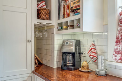 Photo of a small traditional u-shaped separate kitchen in Other with a farmhouse sink, beaded inset cabinets, white cabinets, wood benchtops, white splashback, ceramic splashback, white appliances, medium hardwood floors and no island.