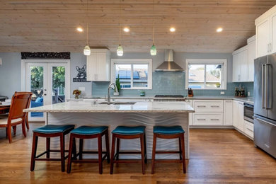 Example of a beach style l-shaped medium tone wood floor and shiplap ceiling open concept kitchen design in Other with an undermount sink, shaker cabinets, white cabinets, quartz countertops, blue backsplash, glass tile backsplash, stainless steel appliances and an island