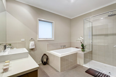 This is an example of a mid-sized traditional 3/4 bathroom in Melbourne with recessed-panel cabinets, dark wood cabinets, a drop-in tub, a corner shower, beige tile, porcelain tile, beige walls, porcelain floors, an integrated sink, granite benchtops, beige floor, a hinged shower door, white benchtops, a niche, a single vanity and a built-in vanity.