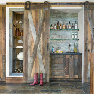 デンバーの小さいラスティックスタイルのおしゃれなウェットバー (アンダーカウンターシンク、シェーカースタイル扉のキャビネット、ヴィンテージ仕上げキャビネット、御影石カウンター、グレーのキッチンパネル、石スラブのキッチンパネル、スレートの床、茶色い床、黒いキッチンカウンター) の写真