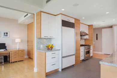Photo of a large modern galley eat-in kitchen in Vancouver with flat-panel cabinets, white cabinets, grey splashback, stone slab splashback, stainless steel appliances and light hardwood floors.