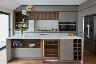 Large contemporary grey and brown l-shaped open plan kitchen in London with a built-in sink, flat-panel cabinets, grey cabinets, quartz worktops, grey splashback, engineered quartz splashback, stainless steel appliances, medium hardwood flooring, an island, grey worktops and feature lighting.