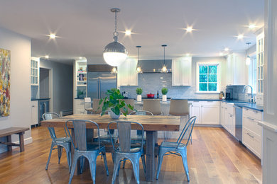 Example of a large transitional l-shaped medium tone wood floor and brown floor eat-in kitchen design in Boston with a farmhouse sink, shaker cabinets, white cabinets, quartz countertops, gray backsplash, stainless steel appliances, an island and glass tile backsplash