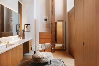 This is an example of a large contemporary master bathroom in Chicago with white walls, light hardwood floors, beige floor, exposed beam, brick walls, furniture-like cabinets, medium wood cabinets, a freestanding tub, a wall-mount toilet, white tile, cement tile, an integrated sink, quartzite benchtops, white benchtops, a single vanity and a floating vanity.