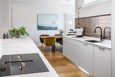 Offene, Zweizeilige Stilmix Küche mit Doppelwaschbecken, Küchenrückwand in Metallic, braunem Holzboden und weißer Arbeitsplatte in München