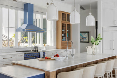 Kitchen - coastal l-shaped kitchen idea in Tampa with a farmhouse sink, recessed-panel cabinets, white cabinets, white backsplash, stone slab backsplash, colored appliances, an island and white countertops