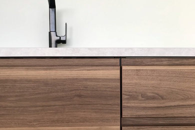 Cette image montre une petite cuisine ouverte linéaire design en bois brun avec un évier 1 bac, un placard à porte affleurante, un plan de travail en béton, une crédence blanche, une crédence en feuille de verre, sol en béton ciré, aucun îlot, un sol gris et un plan de travail gris.